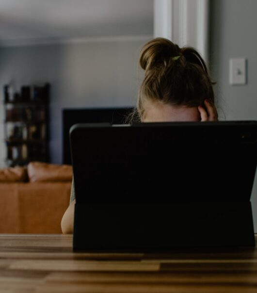 woman in white tank top sitting on chair using black laptop computer